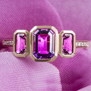 Rose gold three-stone ring set with emerald cut amethysts.