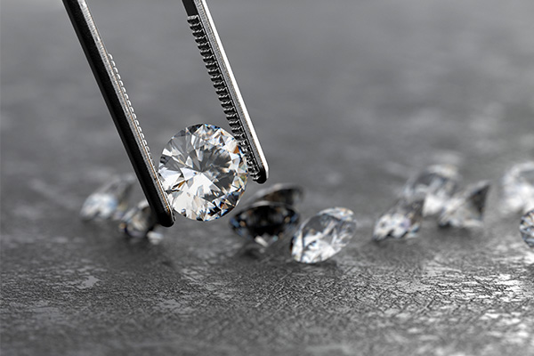 a close up image of a diamond being held with reverse tweezers. loose diamonds are visible in the background.
