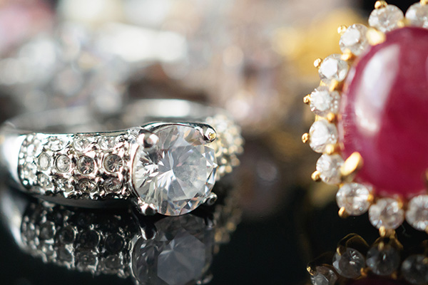 a close up image of a ruby ring and a diamond ring resting on a black reflective surface.