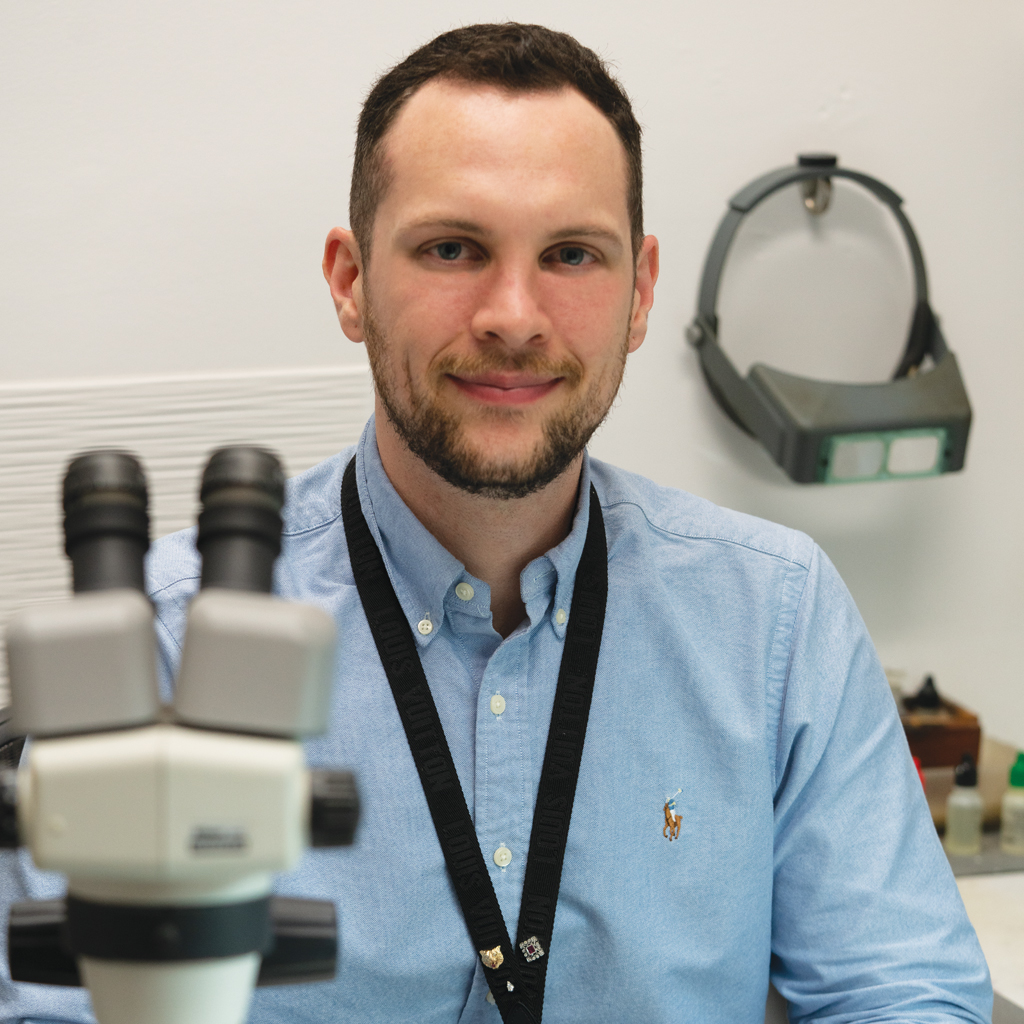 Man in blue shirt with microscope and magnifying visor in gemological laboratory